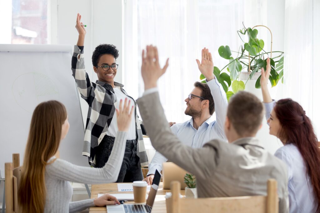 Team members in a meeting happily raising their hands, illustrating how to make your audience feel connected and engaged.