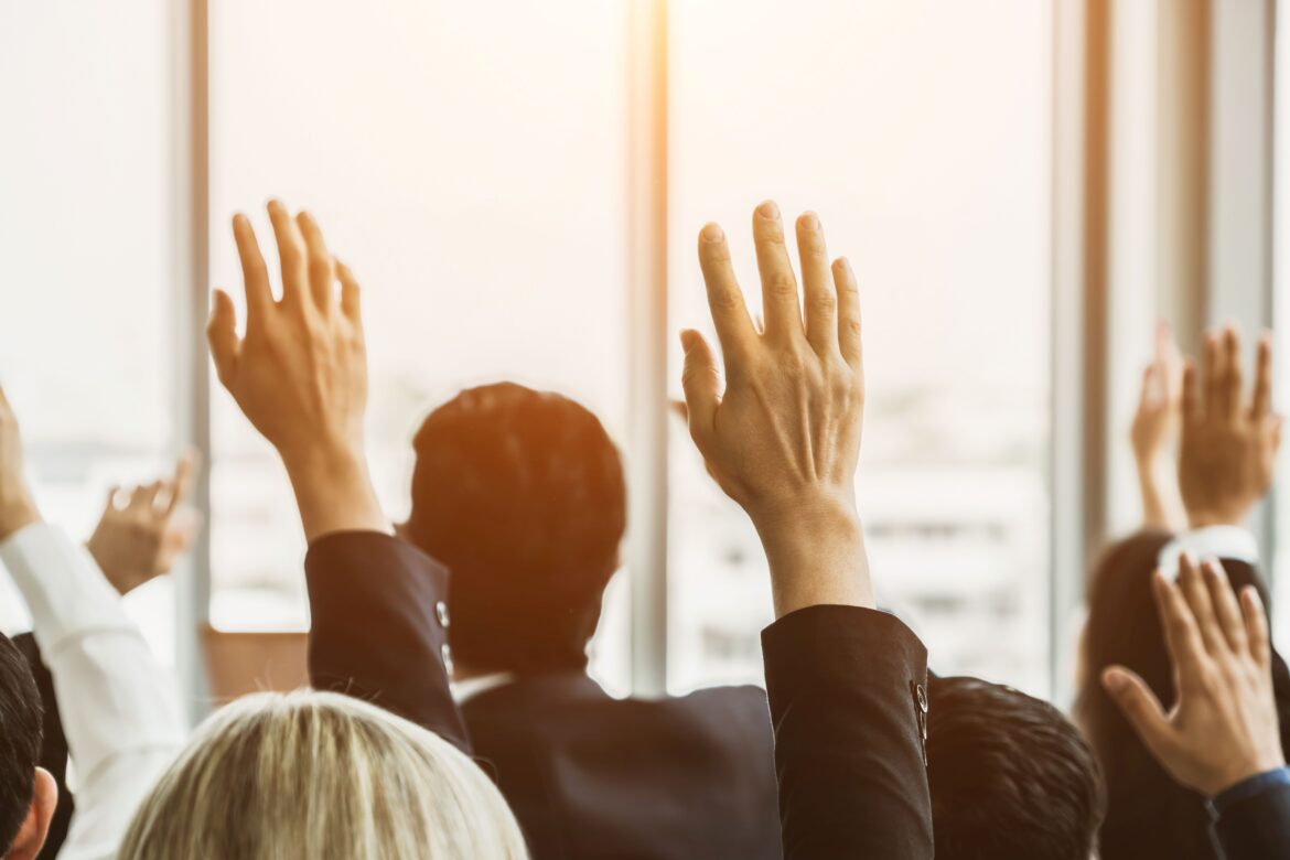 Audience members raising their hands enthusiastically during a presentation, showing how to make your audience feel connected and engaged.