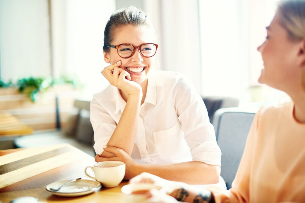 A woman smiling while talking to her friend, fully engaged in the conversation. A great example of how to be more present daily and build deeper connections.