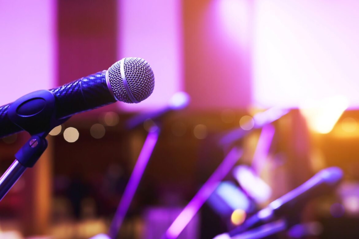 Close-up of microphone on stage lighting at concert hall or conference room, representing how to train your voice for public speaking with confidence and clarity.