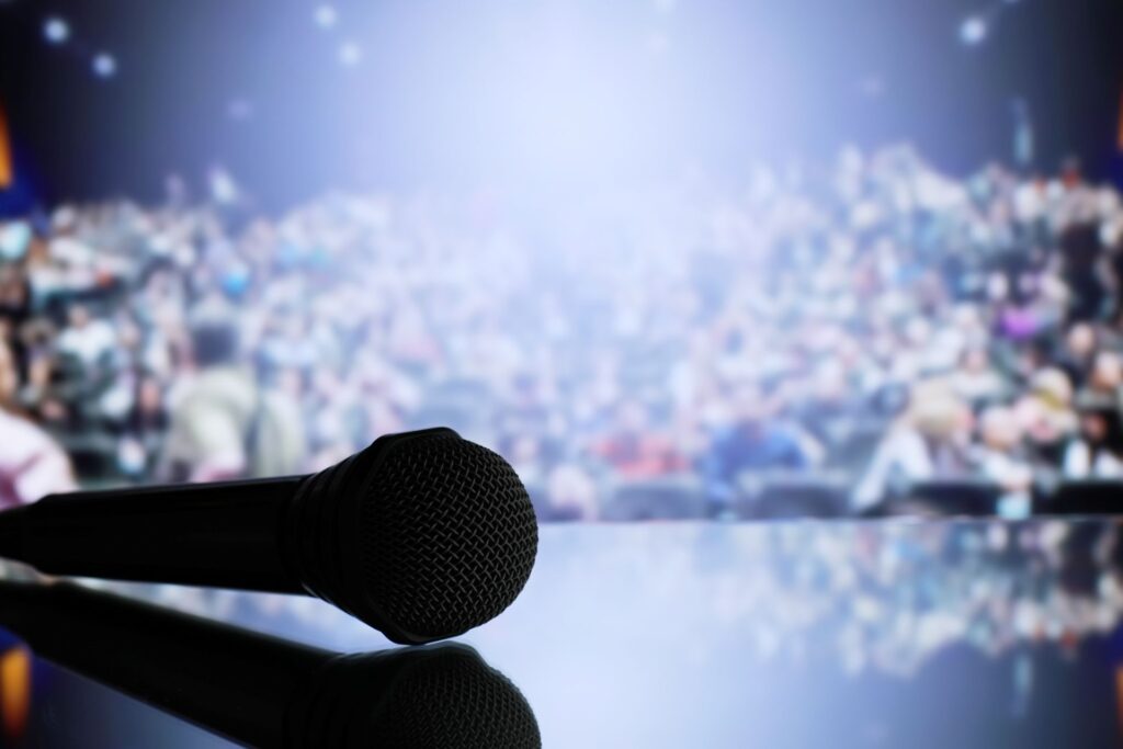 Microphone on stage facing a full auditorium—setting the scene for a speaker ready to hook your audience from the very first moment.
