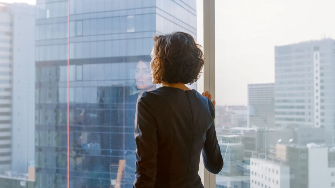 Confident businesswoman standing thoughtfully in her office, embodying what it means to own the room through quiet presence and self-assurance.